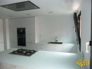 Cocina de diseño con muebles blancos e isla central con bancada en cristal de alta resistencia en Valencia
