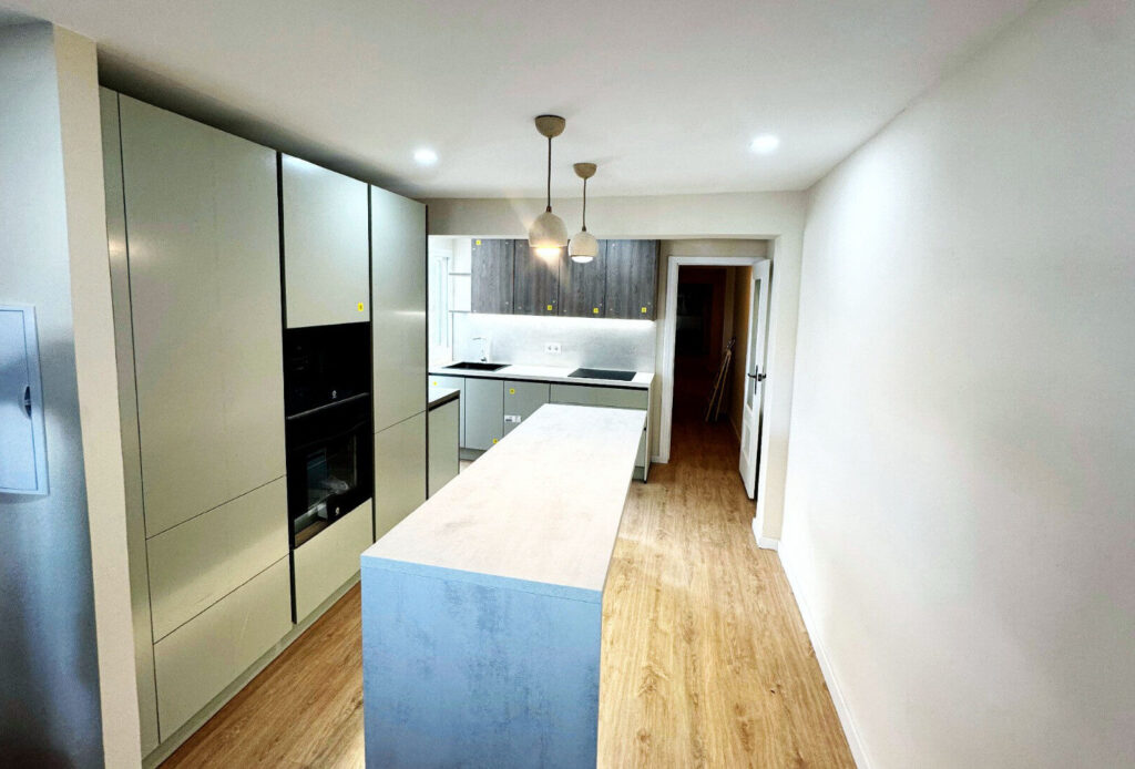 Cocina abierta hacia comedor con gran isla aprovechando la línea del antiguo pasillo.  GAlería al fondo a la izquierda de esta foto