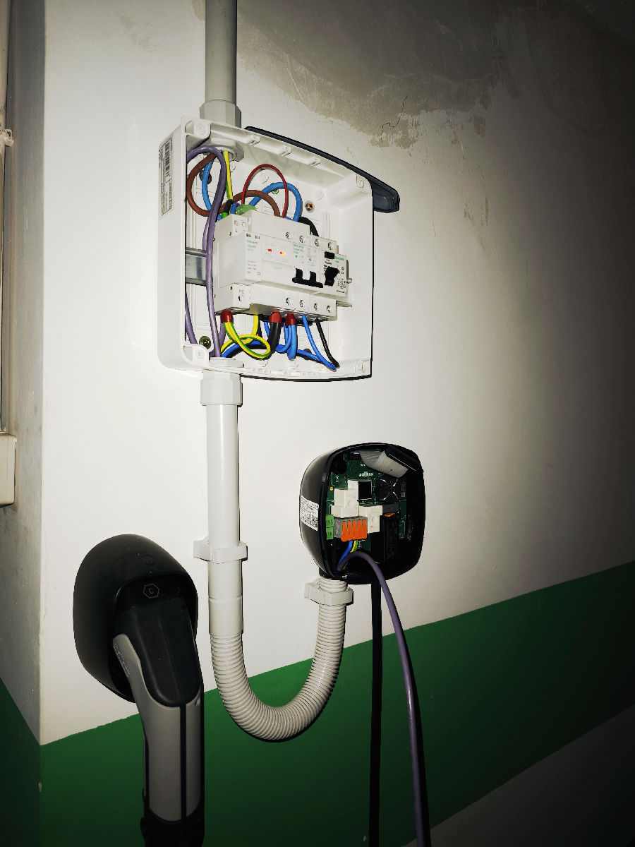 Detalle de pequeño cuadro eléctrico, punto de carga y manguera en plaza de garaje en un parking comunitario en finca de Valencia